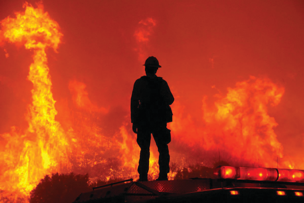A U.S. Forest Service firefighter stands atop his engine to monitor conditions as his fellow firefighters operate during a firestorm in California. An early and busy wildland fire season is already putting emergency resources to the test.