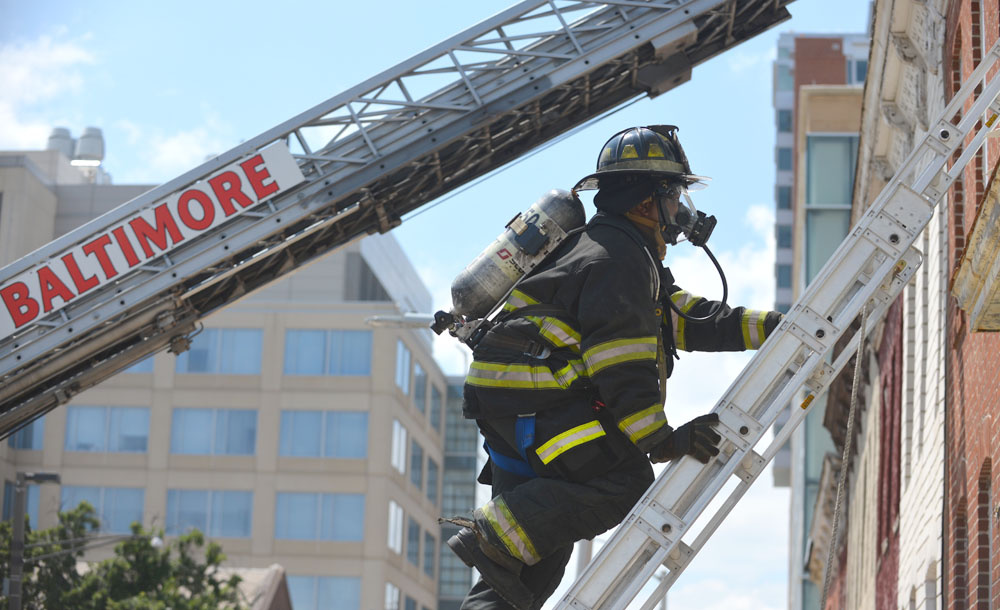 A firefighter climbs a ladder during a truck company operations class in a row of vacant homes in Baltimore Tuesday.