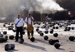 Firefighters walk through the blast site littered with tanks. Firefighters walk through the blast site littered with tanks.