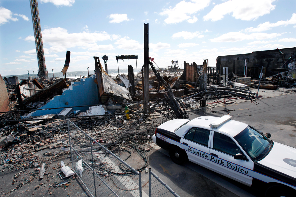 A Seaside Park police officer sits in his cruiser near the charred rubble in Seaside Park, N.J., Tuesday, Sept. 17, 2013, after a fire last Thursday that started near a frozen custard stand in Seaside Park, quickly spread north into neighboring Seaside Heights. More than 50 businesses in the two towns were destroyed. The massive boardwalk fire in New Jersey began accidentally, the result of an electrical problem, an official briefed on the investigation said Tuesday.