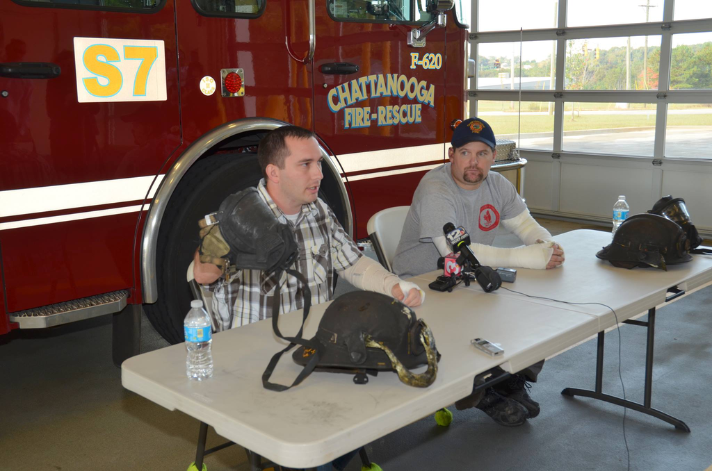 Senior Firefighter Dan Peterson (left) shows the charred face mask he was wearing inside the fire as Firefighter Chad Williams watches.