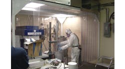 Employee wearing personal protective equipment works in an enclosure while handling powder-form nanomaterials.