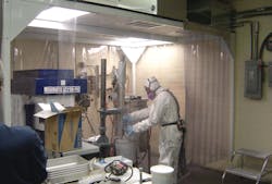 Employee wearing personal protective equipment works in an enclosure while handling powder-form nanomaterials. Employee wearing personal protective equipment works in an enclosure while handling powder-form nanomaterials.