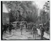This undated photo shows a Hearst Metrotone News crew filming a silent newsreel featuring a building fire. The company was renamed News of the Day in 1916. It is interesting to note the wooden platform being used by one cameraman. It is not clear whether the fire was staged.