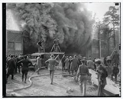 This undated photo shows a Hearst Metrotone News crew filming a silent newsreel featuring a building fire. The company was renamed News of the Day in 1916. It is interesting to note the wooden platform being used by one cameraman. It is not clear whether the fire was staged.