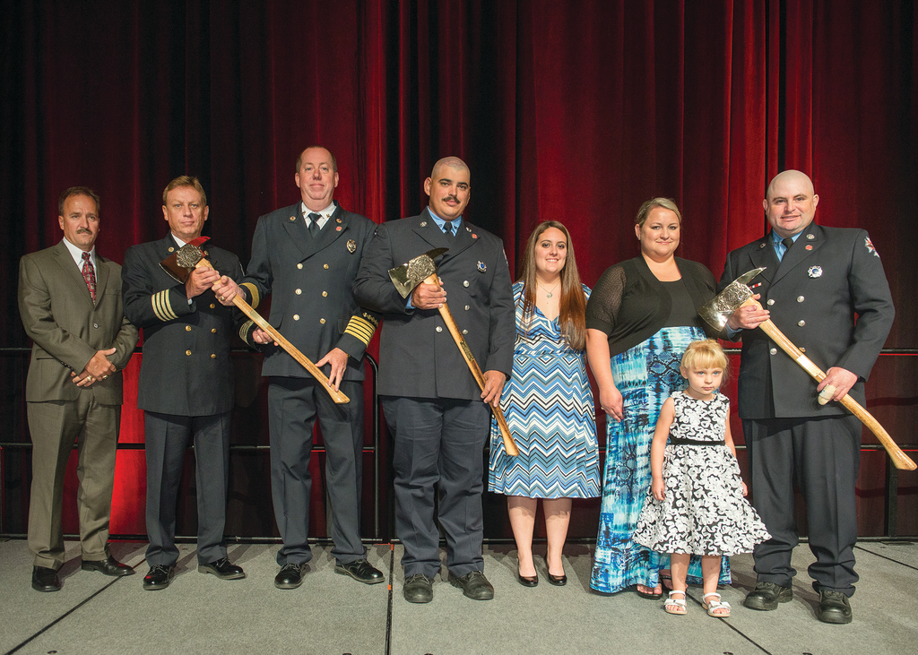 The Firehouse&circledR; Magazine Heroism Awards program honored members of the Bryan, TX, Fire Department during the Opening Ceremonies at Firehouse Expo 2014 in Baltimore, MD, in July. From left to right: Bryan City Manager Kean Register; Assistant Chief Terry Barnett; Fire Chief Randy McGregor; Firefighter Mitchel Moran and his fiancee, Katy Garcia; Kara Mantey and Kanzie Mantey, wife and daughter of Firefighter Ricky Mantey; and Mantey. Lieutenant Greg Pickard was honored posthumously.