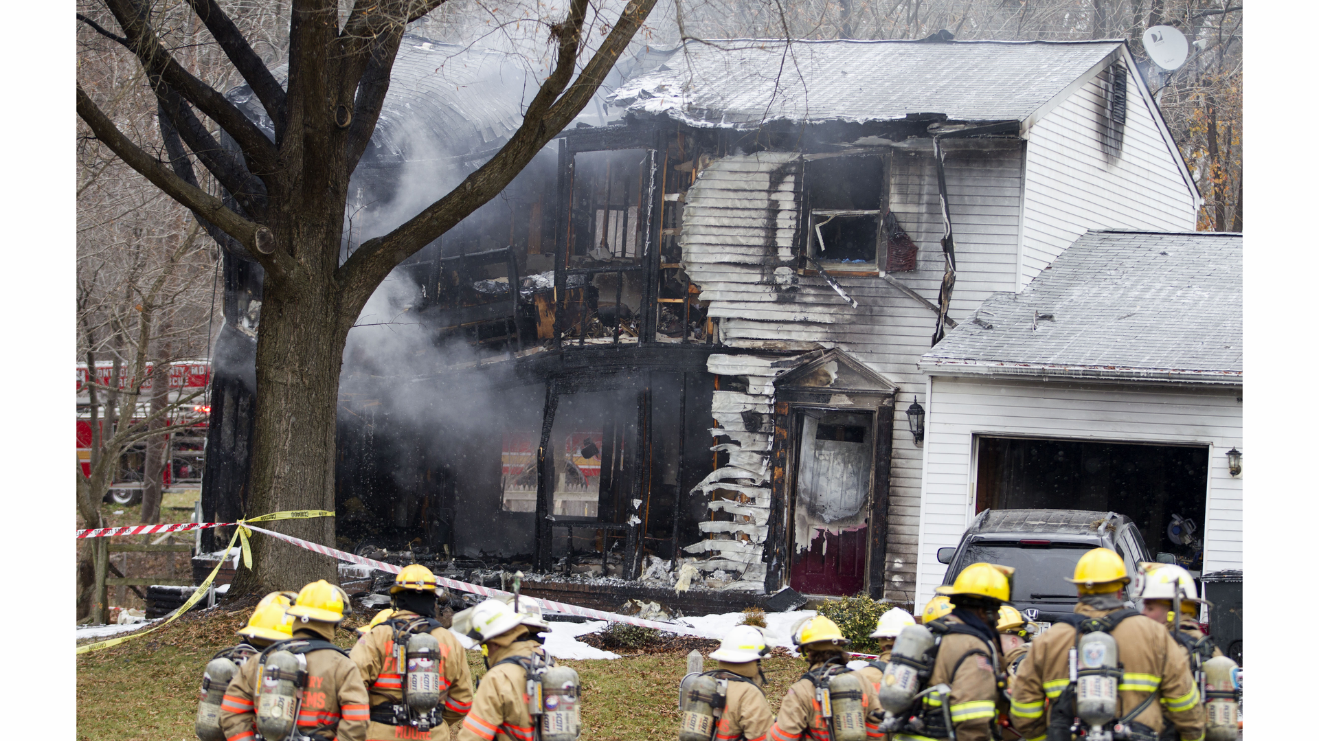Firefighters gather outside one of the homes destroyed after a plane crash.