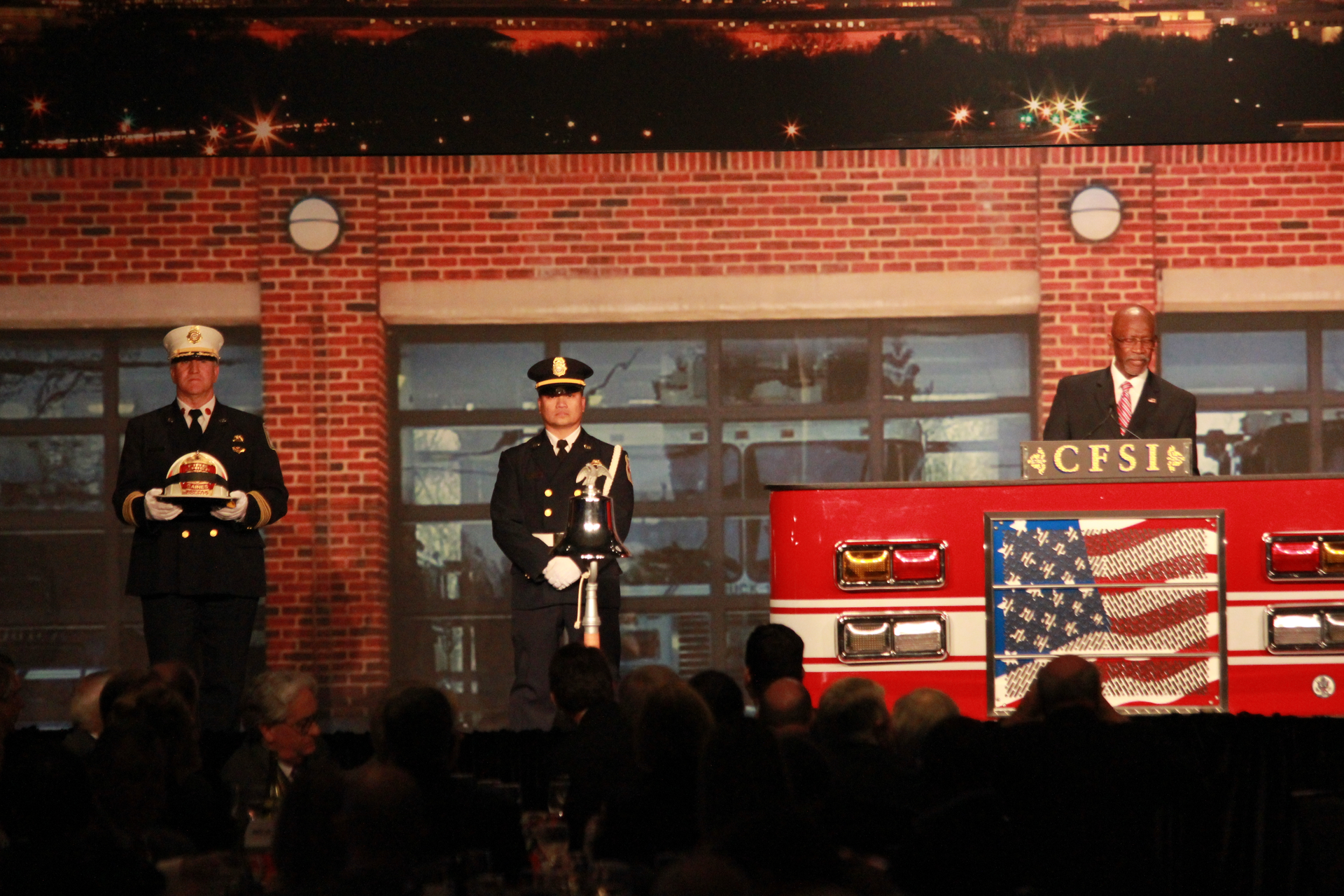 U.S. Fire Administrator Ernie Mitchell, at podium, remembers Glenn Gaines, while Fairfax County, Va. Chief Richie Bowers holds his helmet.