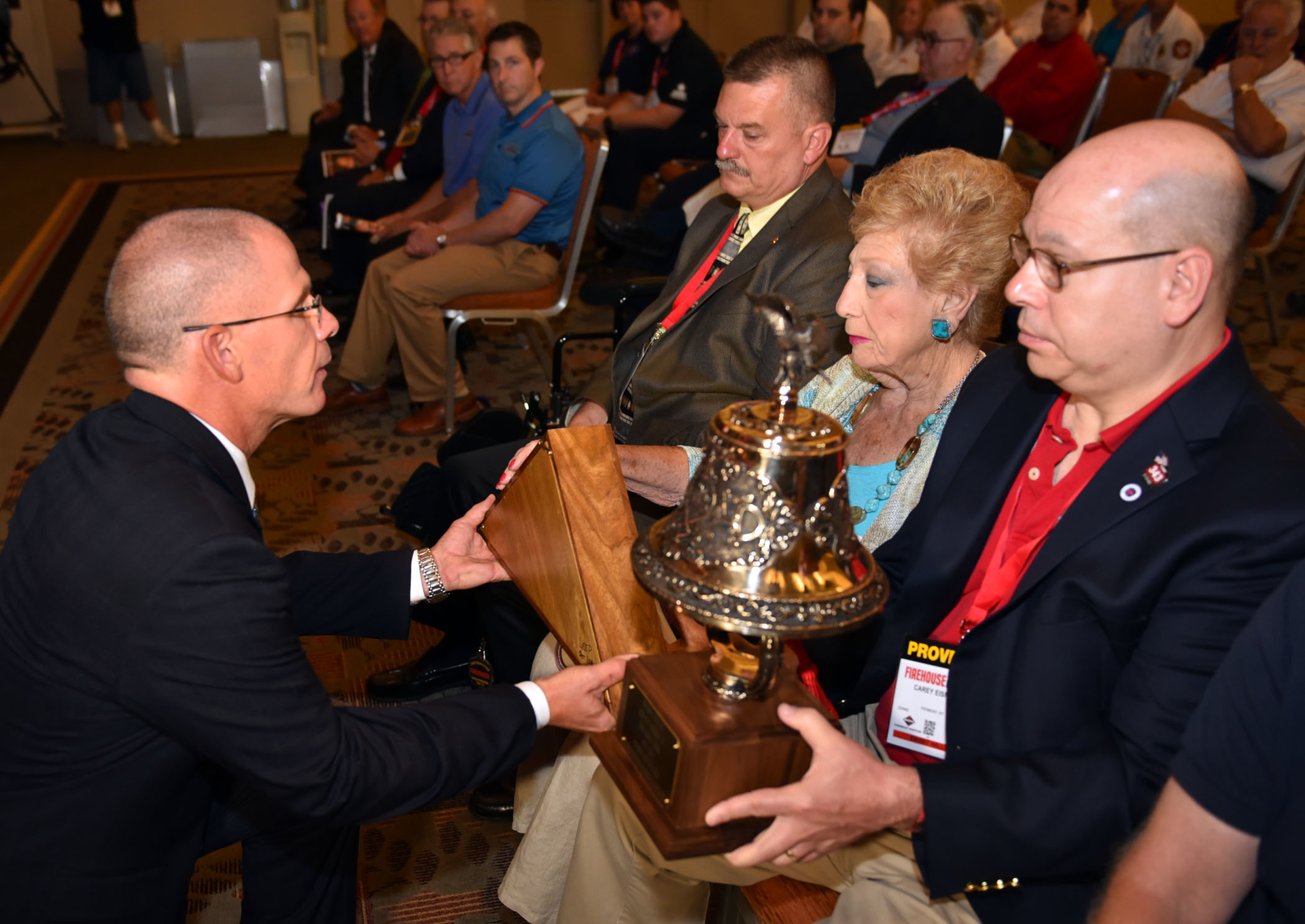 Firehouse Editor-in-Chief Tim Sendelbach presents a memorial bell and American Flag to Harvey Eisner's brother Carey, right, and mother Carol.