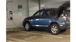 This electric plug-in vehicle is in a public parking garage. It is plugged into the wall-mounted charging station. A fire is evident at the end of the charging cable where it is connected to the charging receptacle on the vehicle. Recommended tactics include: Isolate and secure the immediate area, request power shutdown, protect exposures, chock wheels of vehicle if safe to do so, and initiate additional activities as appropriate once power is confirmed shut off to the charging station.