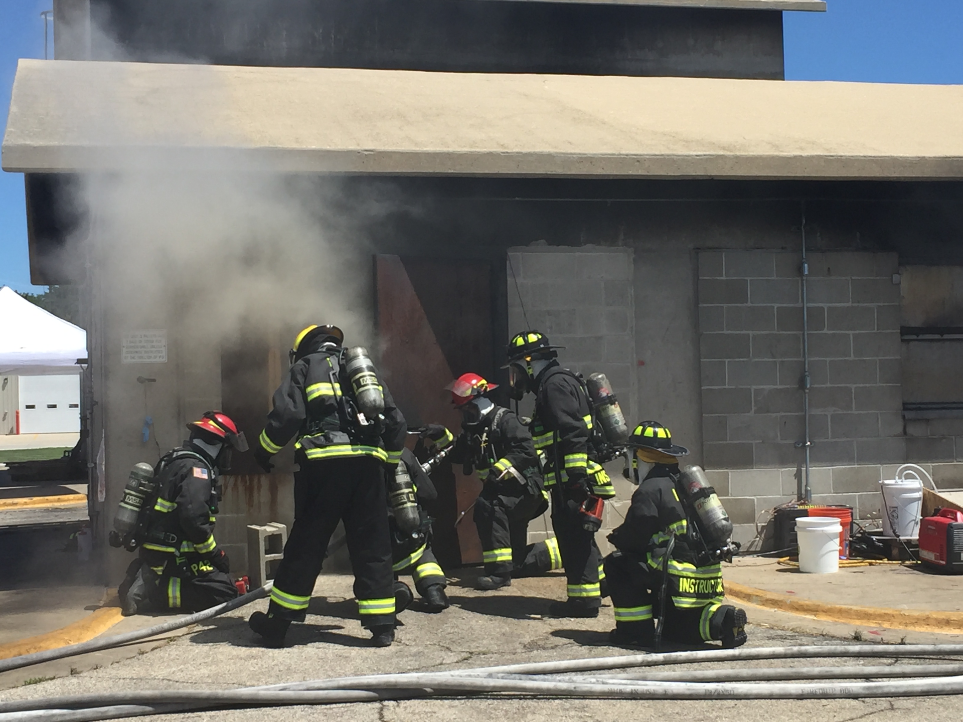 The group of firefighters and instructors prepare to enter the burn building. Each firefighter is wearing a puck that helps collect data on heart rate and other physical measurements.