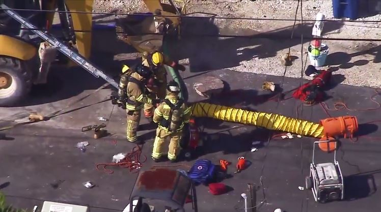 Firefighters work at the scene where three workers died and one firefighter was overcome by fumes inside a manhole in Lake Surprise.