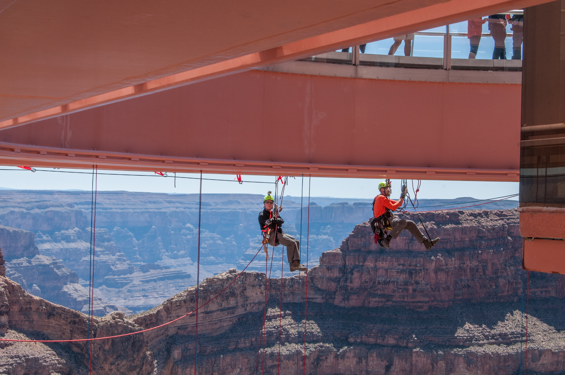 Two level III rope access technicians meet at the halfway point pre-rigging protection lines under the Grand Canyon Skywalk. The Skywalk is a glass walkway cantilever bridge built over the Grand Canyon in 2007. The underside of the glass had never been cleaned, and Abseilon USA was contracted to do this high-exposure job.