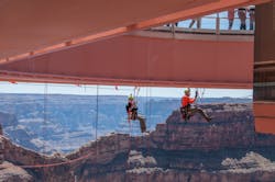 Two level III rope access technicians meet at the halfway point pre-rigging protection lines under the Grand Canyon Skywalk. The Skywalk is a glass walkway cantilever bridge built over the Grand Canyon in 2007. The underside of the glass had never been cleaned, and Abseilon USA was contracted to do this high-exposure job.