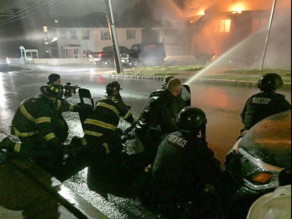 Chelsea firefighters are protected by SWAT officers with shields while trying to to douse a fire set Monday night by a man engaged in an hours-long armed standoff with police.