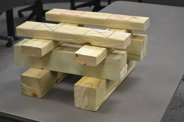 Markings on the top layer of this training cribbing indicate the 12 1/4 square inches of load-bearing contact at each of the four points on this 2 x 4 and 4 x 4 double-box crib. Multiplying 12 1/4 x 500 psi gives this soft wood box crib its 24,500-pound capacity when all four contact points are evenly loaded. Each wood piece is positioned so the load is applied perpendicular or in a cross-grain fashion. Also note the 3 1/2-inch end &ldquo;overhang&rdquo; of each layer in the stack. Photo by Ron Moore