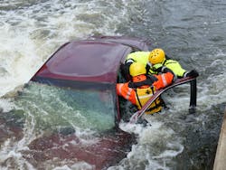 Rescuers who access the car by wading or swimming can break out windows and also open doors on the downstream (in the eddy) side. Notice that the roof is dented in, the first rescuer swimming to the car should tell the victims that he is going to dent the roof in. This provides a safer work area. Rescuers who access the car by wading or swimming can break out windows and also open doors on the downstream (in the eddy) side. Notice that the roof is dented in, the first rescuer swimming to the car should tell the victims that he is going to dent the roof in. This provides a safer work area.