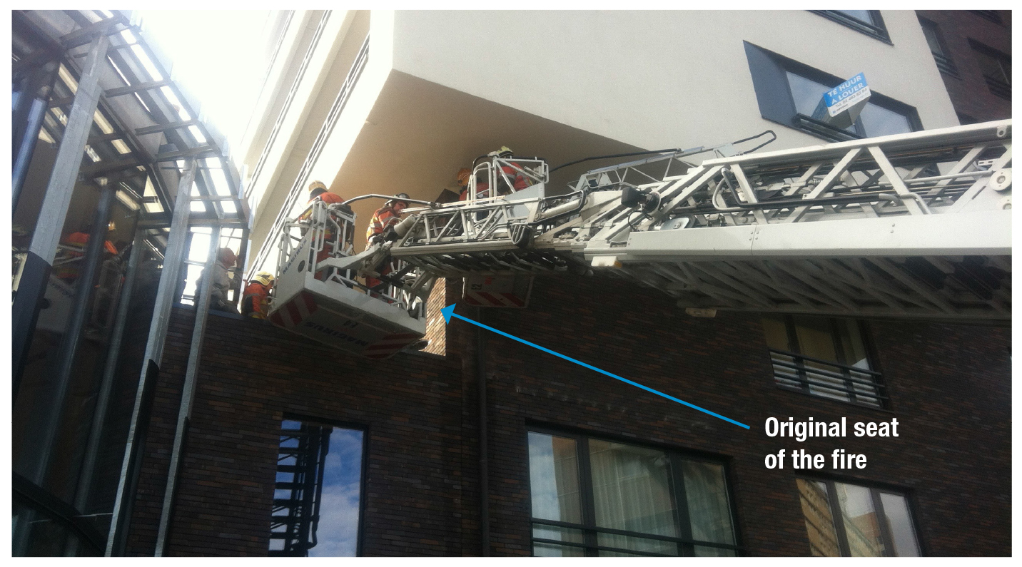 The ladder crew working where the fire started. The section of wall indicated with the bottom blue arrow is about 2 meters wide. The fire could pass the corner and create fire extension across the entire brick wall.