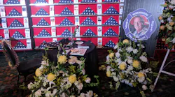 A tribute to Chief Alan V. Brunacini includes an empty chair facing a wall of flags of fallen firefighters.