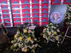 A tribute to Chief Alan V. Brunacini includes an empty chair facing a wall of flags of fallen firefighters.