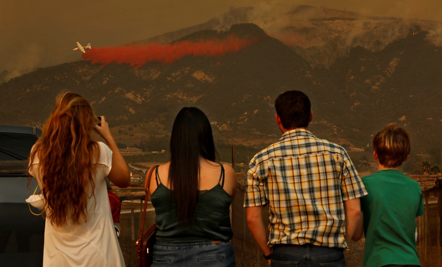 Onlookers watch as a tanker drops flame retardant material on hot spots in Carpenteria, CA, on Dec. 11, 2017, during efforts to contain the Thomas Fire.