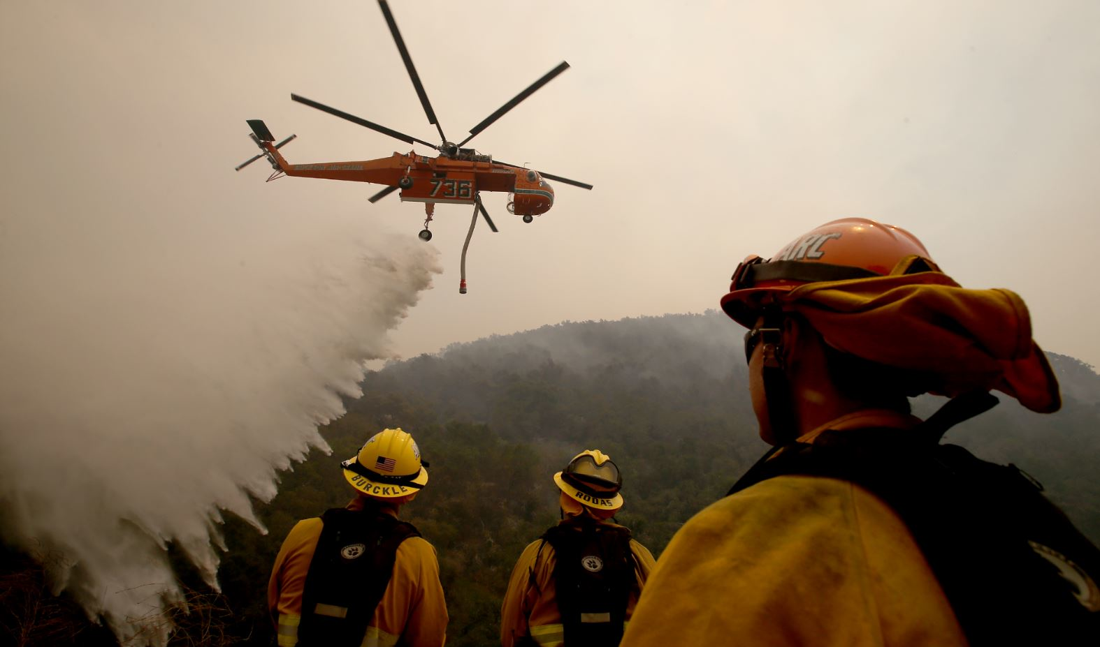 Firefighters look on as a helicopter drops water on the Alamo fire near Santa Maria, CA, on July 8, 2017.