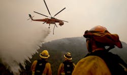 Firefighters look on as a helicopter drops water on the Alamo fire near Santa Maria, CA, on July 8, 2017.