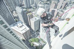 A rope access technician is suspended over the edge of a Chicago skyscraper.