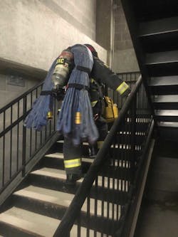 Brandon Anderson taking the stairs in full PPE and with a bundle of hose on his back during training.