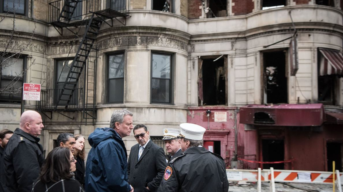 New York City Mayor Bill de Blasio, in blue windbreaker, and FDNY Commissioner Daniel Nigro, wearing tinted glasses, at the scene of a fire in Harlem on March 22, 2018, that killed FDNY Lt. Michael Davidson.