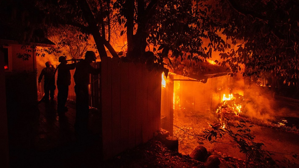 Three firefighters hose down a structure on Ridge Drive to slow the spread of the Carr Fire to other structures on July 26, 2018, in Redding, CA.