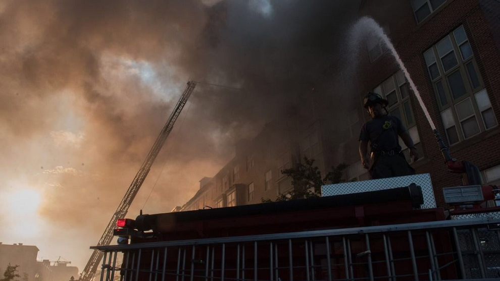 A DC firefighter stands atop a rig as water is poured on a large fire that broke out at a senior apartment complex on Wednesday, Sept. 18, 2018.
