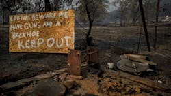 A sign warning looters sits in the foreground of burned properties on Friday, Nov. 16, 2018, in the aftermath of the Camp Fire that tore through Paradise, CA.