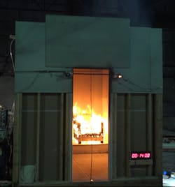 Still frames of the ISO 9705 Test Room burn tests for no flame retardant (NFR, shown here), organophosphate flame retardant (OPFR), reactive flame retardant (RFR), and no flame retardant with barrier textile (BNFR) chairs at 14 minutes from ignition.