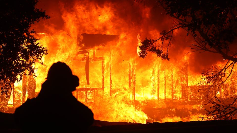 A firefighter stands in the foreground while a home burns as the Kincade Fire moves through Geyserville, CA on Oct. 24, 2019.
