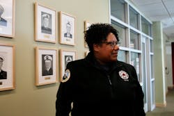 Portland Fire Chief Sara Boone stands in front of a wall of portraits of fire bureau chiefs at Portland Fire Station 1.