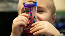 Carter Severs, 5, looks through a glass toy with pink and blue goo inside that floats around, similar to a lava lamp. The tool is part of new autism sensory kits, called Carter Kits after the boy.