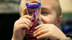 Carter Severs, 5, looks through a glass toy with pink and blue goo inside that floats around, similar to a lava lamp. The tool is part of new autism sensory kits, called Carter Kits after the boy.