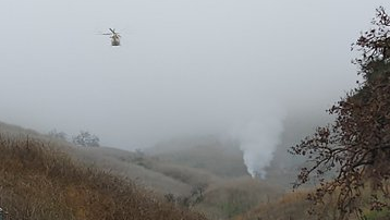 A helicopter crashed and burst into flames, igniting a brush fire, in the hills above Calabasas, CA, on Sunday.
