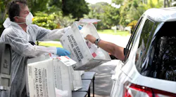 Jill Blasenstein picks up gloves, masks, and hand sanitizer from retired Boynton Beach, FL, firefighter and paramedic Luis Garcia at his home-based drive-through service.