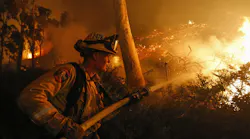 A CAL FIRE firefighter hoses a hillside along Highway 76 in Bonsall, CA, during operations against the Lilac Fire in December 2017.