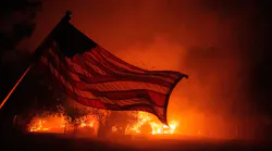 An American flag blows in the wind in front of a burning home in Vacaville, CA, as the LNU Lightning Complex fire burns in the background on Aug. 19, 2020.