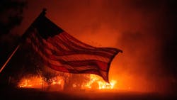 An American flag blows in the wind in front of a burning home in Vacaville, CA, as the LNU Lightning Complex fire burns in the background on Aug. 19, 2020.