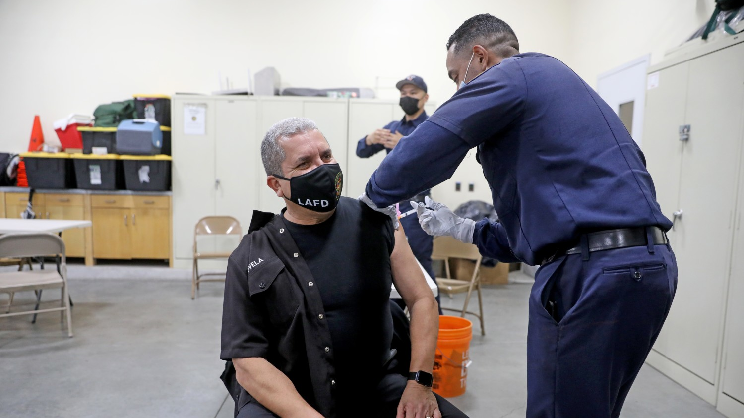 Los Angeles Fire Department fire inspector John Novela (left) receives a Moderna COVID-19 vaccination given by Mario Guillen, a firefighter paramedic, at Station 4 on Dec. 28.