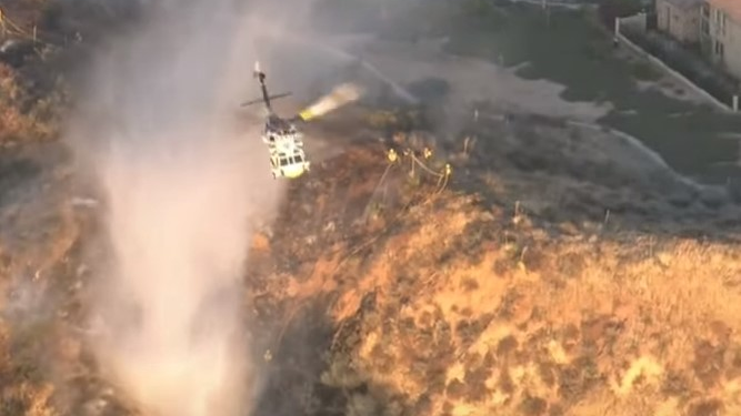 Los Angeles County firefighters battled a brush that erupted following an explosion at a Santa Clarita industrial park that critically injured three people Tuesday.