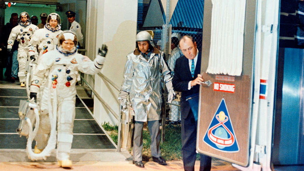 On Dec. 21, 1968, the Apollo 8 crew leaves the Kennedy Space Center's then-named Manned Spacecraft Operations Building during the mission's prelaunch countdown on the way to their history-making lunar orbiting flight. Commander Frank Borman (waving) leads the crew, followed by astronauts Jim Lovell, command module pilot; and William Anders, lunar module pilot.