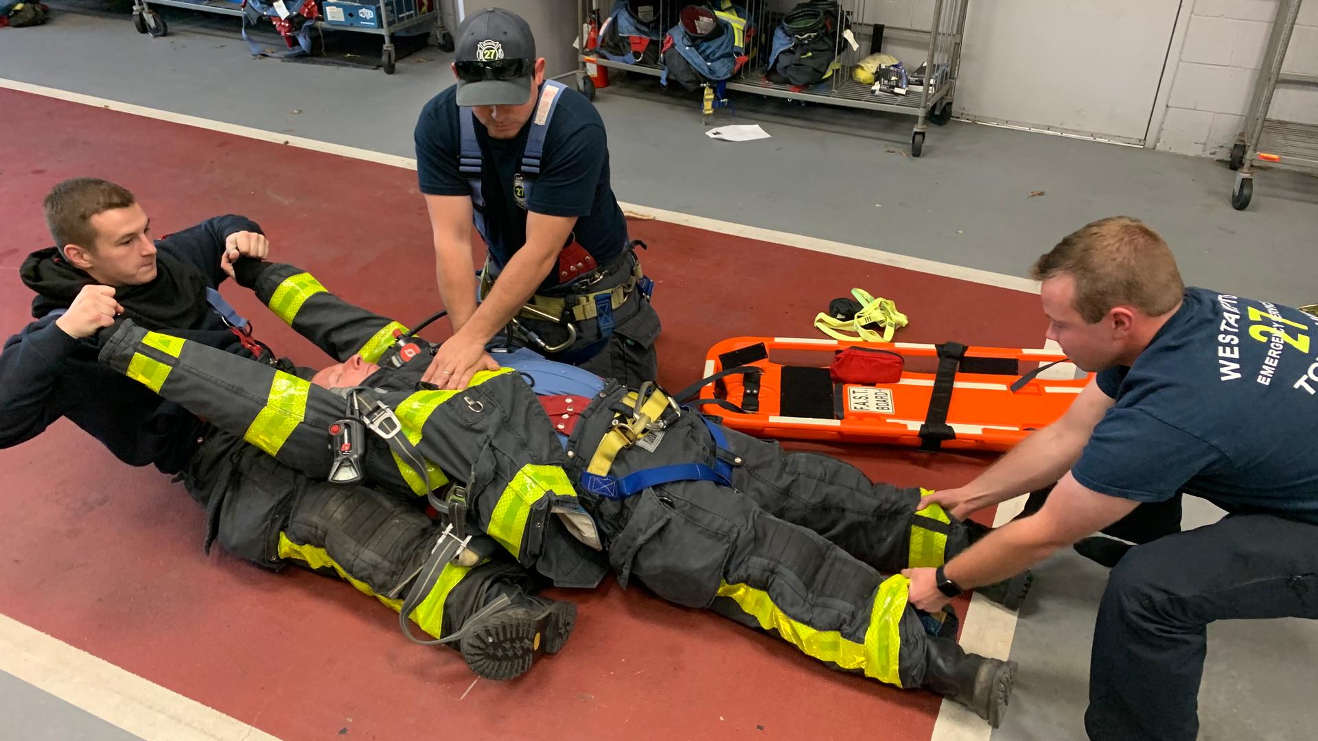Firefighters in their turnout gear train on extricating a firefighter who is in cardiac arrest.