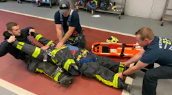 Firefighters in their turnout gear train on extricating a firefighter who is in cardiac arrest.