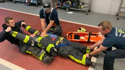 Firefighters in their turnout gear train on extricating a firefighter who is in cardiac arrest.