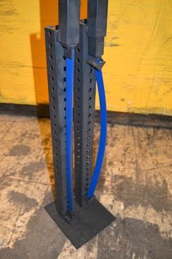 Photo 1: To show that flexible end fittings, such as a hinged base, can make a difference in a strut’s working load limit, equal weights were placed at the top of each steel band. (The band on the right has V-shaped end fixtures at the top and is wide open at the bottom. The band on the left has rigid, fixed end fittings.) The steel band that has the rigid end fittings (similar to fixed ends for struts that are used in a trench rescue application) holds up well. The other band buckles under the same weight. Without rigid ends, the steel band is allowed to move and flex under the load. Photo 1: To show that flexible end fittings, such as a hinged base, can make a difference in a strut’s working load limit, equal weights were placed at the top of each steel band. (The band on the right has V-shaped end fixtures at the top and is wide open at the bottom. The band on the left has rigid, fixed end fittings.) The steel band that has the rigid end fittings (similar to fixed ends for struts that are used in a trench rescue application) holds up well. The other band buckles under the same weight. Without rigid ends, the steel band is allowed to move and flex under the load.